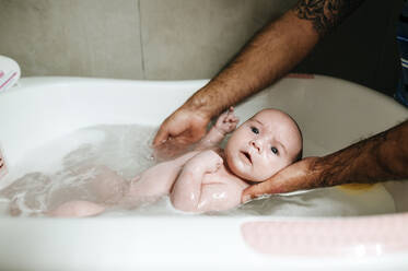 Baby girl bathing, holding by father's hands - KIJF02970