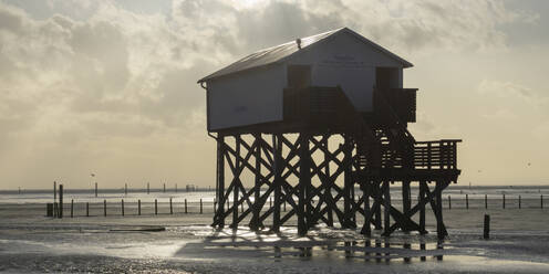 Germany, Schleswig-Holstein, Sankt Peter-Ording, Stilt house standing on coastal beach of North Sea at dusk - WIF04239