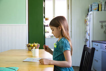 Kleines Mädchen sitzt am Küchentisch und zeichnet einen Osterhasen - LVF08814