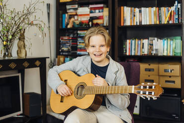 Portrait of happy boy with guitar at home - MJF02443