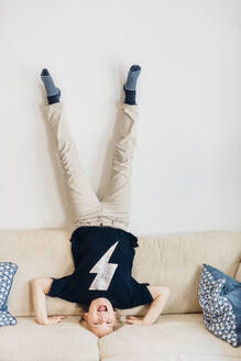 Carefree boy doing a headstand on couch in living room at home - MJF02446