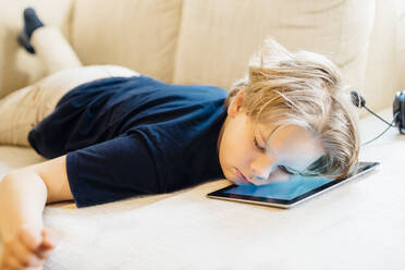 Boy lying on tablet on couch taking a nap - MJF02449