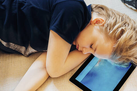 Boy lying on tablet on couch taking a nap stock photo