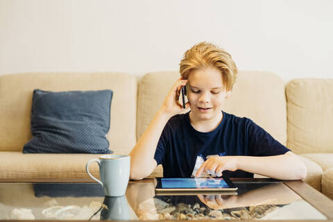 Junge benutzt Smartphone und Tablet im heimischen Wohnzimmer, lizenzfreies Stockfoto