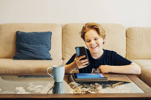 Glücklicher Junge, der Smartphone und Tablet im heimischen Wohnzimmer benutzt, lizenzfreies Stockfoto