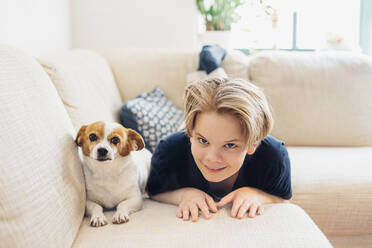 Porträt eines Jungen mit Hund auf der Couch im Wohnzimmer zu Hause - MJF02465
