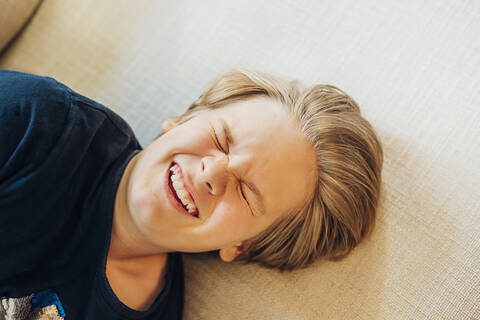 Draufsicht auf einen verspielten Jungen, der auf der Couch liegt, lizenzfreies Stockfoto