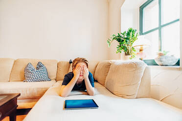 Junge liegt auf der Couch im Wohnzimmer zu Hause und bedeckt seine Augen - MJF02479