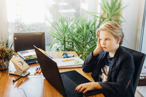 Frustrated boy sitting at desk with laptop stock photo