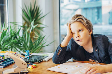 Frustrated boy sitting at desk with workbook - MJF02488