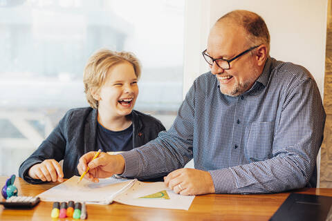 Happy father and son doing homework at desk stock photo