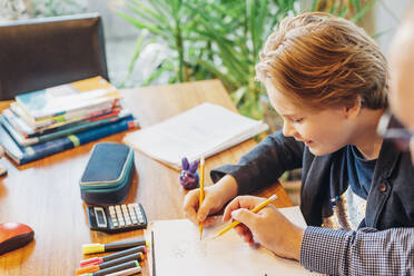 Father helping son doing homework at desk - MJF02499