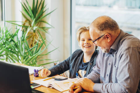 Vater hilft Sohn bei den Hausaufgaben am Schreibtisch, lizenzfreies Stockfoto