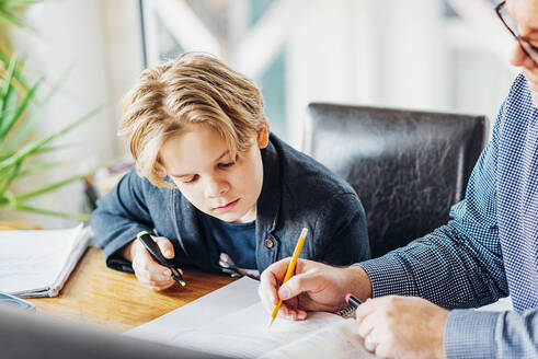 Father helping son doing homework at desk - MJF02507