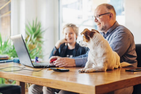 Glücklicher Vater und Sohn zu Hause mit Hund auf dem Schreibtisch, lizenzfreies Stockfoto