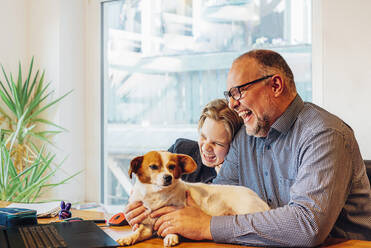 Happy father and son at home with dog on desk - MJF02510