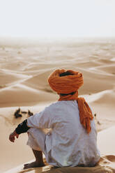 Rückenansicht eines sitzenden Mannes in der Wüste von Merzouga, Marokko - DAMF00345