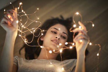 Young woman lying on floor, watching fairy lights - FMKF06159