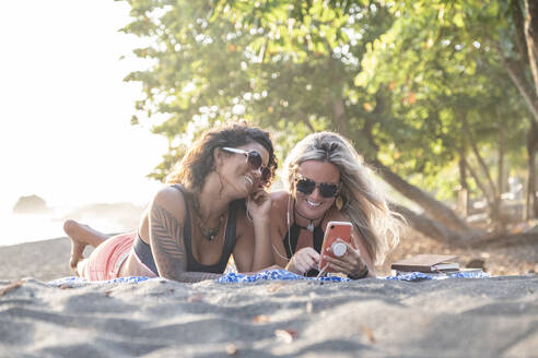 Zwei glückliche Frauen hören Musik am Strand, Costa Rica - AMUF00053