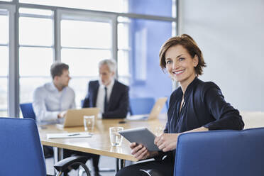 Portrait of smiling businesswoman with tablet during a meeting in office - RORF02110