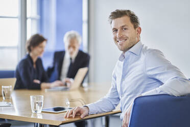 Porträt eines lächelnden Geschäftsmannes während einer Sitzung im Büro - RORF02116