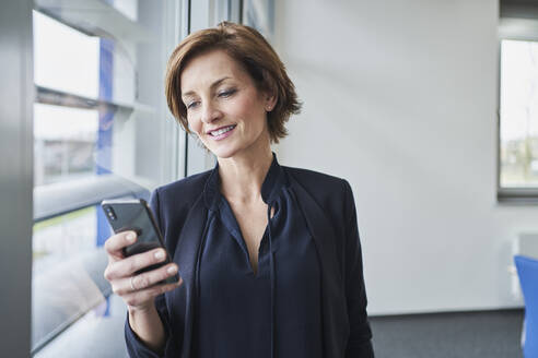 Geschäftsfrau benutzt Mobiltelefon am Fenster - RORF02123