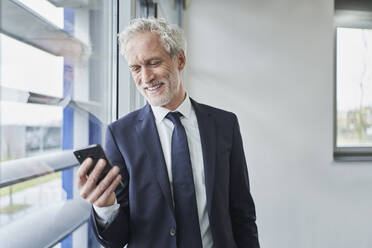 Businessman using cell phone at the window - RORF02131