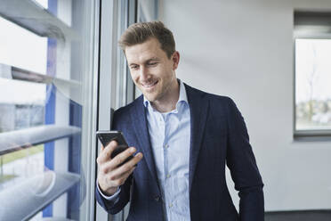 Businessman using cell phone at the window - RORF02137