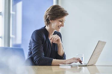 Smiling businesswoman using laptop at desk in office - RORF02142