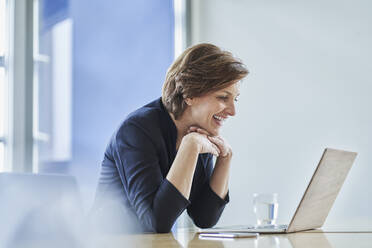 Happy businesswoman using laptop at desk in office - RORF02143