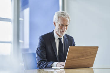 Confident businessman using laptop at desk in office - RORF02149