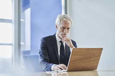 Konzentrierter Geschäftsmann mit Laptop am Schreibtisch im Büro - RORF02152