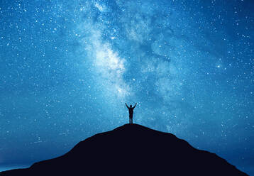 Low Angle View Of Silhouette Man Standing On Mountain Against Blue Star Field At Night - EYF04835