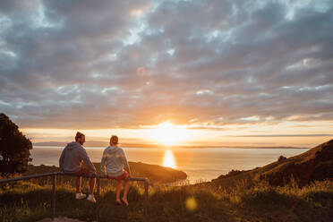 Friends Sitting On Railing Against Sky During Sunset - EYF04874