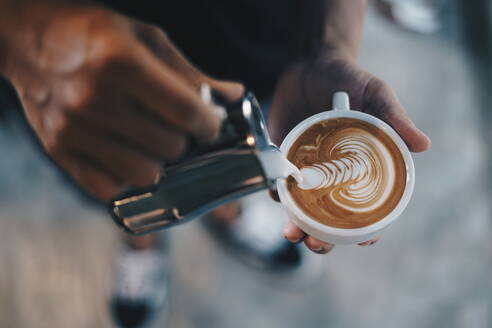 Niedriger Ausschnitt einer Person, die Milch in einen Cappuccino gießt - EYF04907
