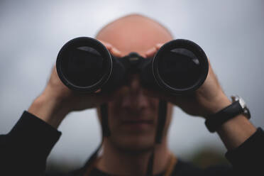 Close-Up Of Mid Adult Man Looking Through Binoculars While Standing Against Sky - EYF04963