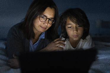 Portrait of mother and son lying together on bed at home looking at digital tablet - VABF02785