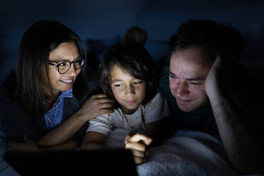 Eltern und Sohn liegen zusammen auf dem Bett zu Hause und benutzen ein digitales Tablet - VABF02787