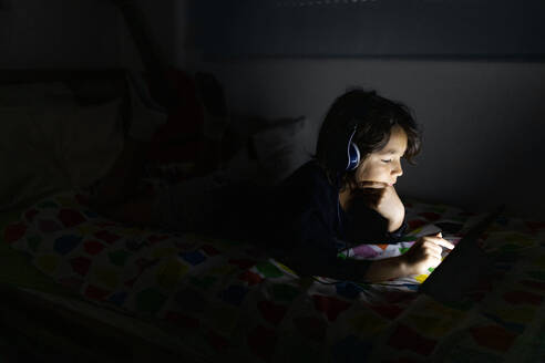 Junge, der zu Hause auf dem Bett liegt und Kopfhörer und ein digitales Tablet benutzt - VABF02790