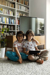 Portrait of two brothers with digital tablet sitting on floor in the living room - VABF02802