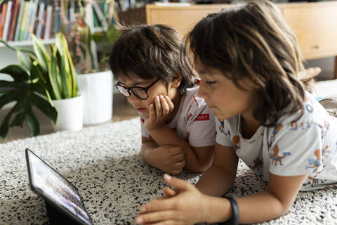 Two brothers lying on the floor at home using digital tablet for video chat with their mother stock photo