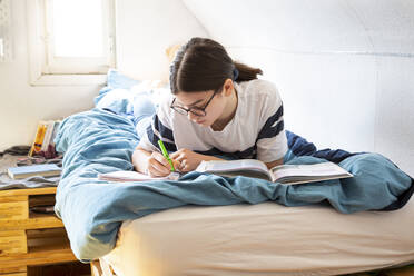 Girl lying on bed doing homework - LVF08816