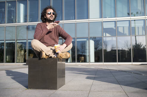 Portrait of bearded man on the phone sitting outdoors with coffee to go - KIJF02973