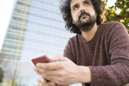 Portrait of bearded man with smartphone outdoors - KIJF02975