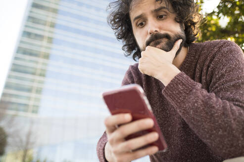 Portrait of bearded man looking at smartphone outdoors - KIJF02976