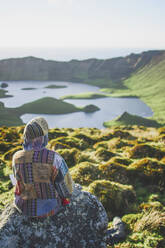 Portugal, Azoren, Junge Frau sitzt auf einem Felsen und bewundert die vulkanische Landschaft von Caldeirao - FVSF00170