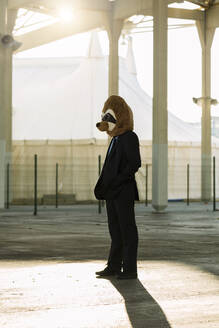 Geschäftsmann im schwarzen Anzug mit Erdmännchen-Maske im Gegenlicht, Barcelona, Spanien - XLGF00028