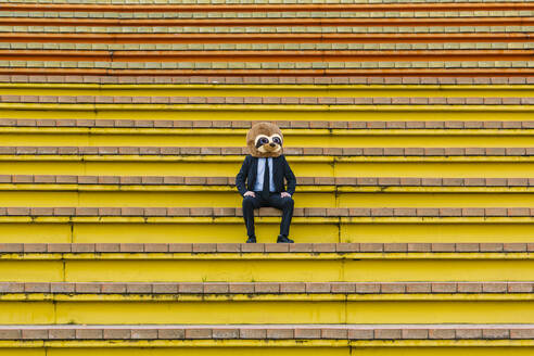 Geschäftsmann im schwarzen Anzug mit Erdmännchenmaske auf einer Treppe sitzend - XLGF00032