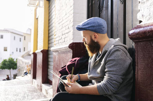 Mann sitzt an der Eingangstür in der Stadt und zeichnet eine Skizze, Granada, Spanien - DGOF00816