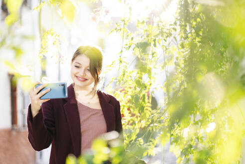 Lächelnde Frau macht ein Selfie in einer malerischen Gasse in der Stadt - DGOF00831